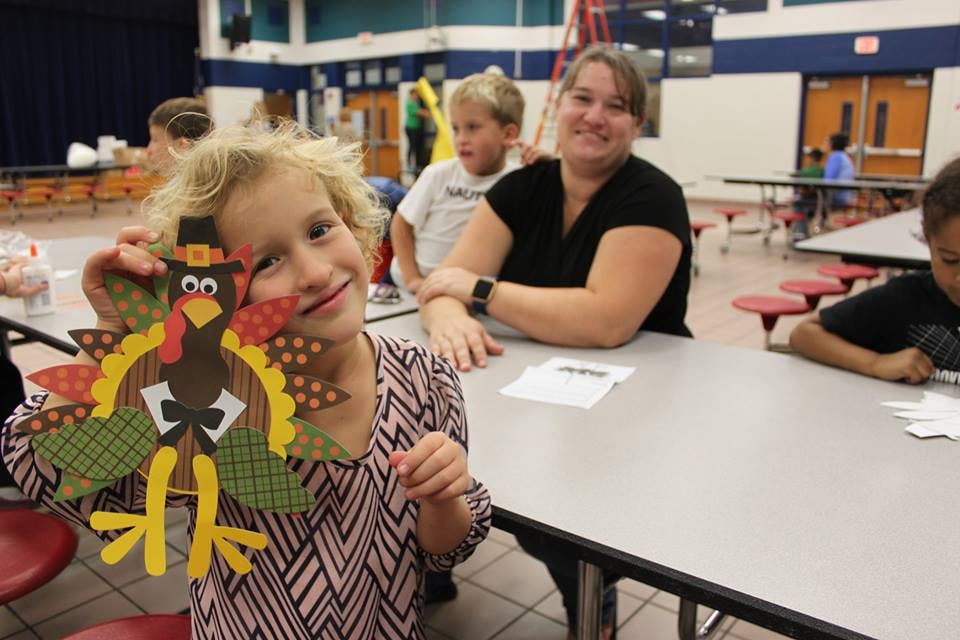 Child holding up a turkey craft in a cafeteria