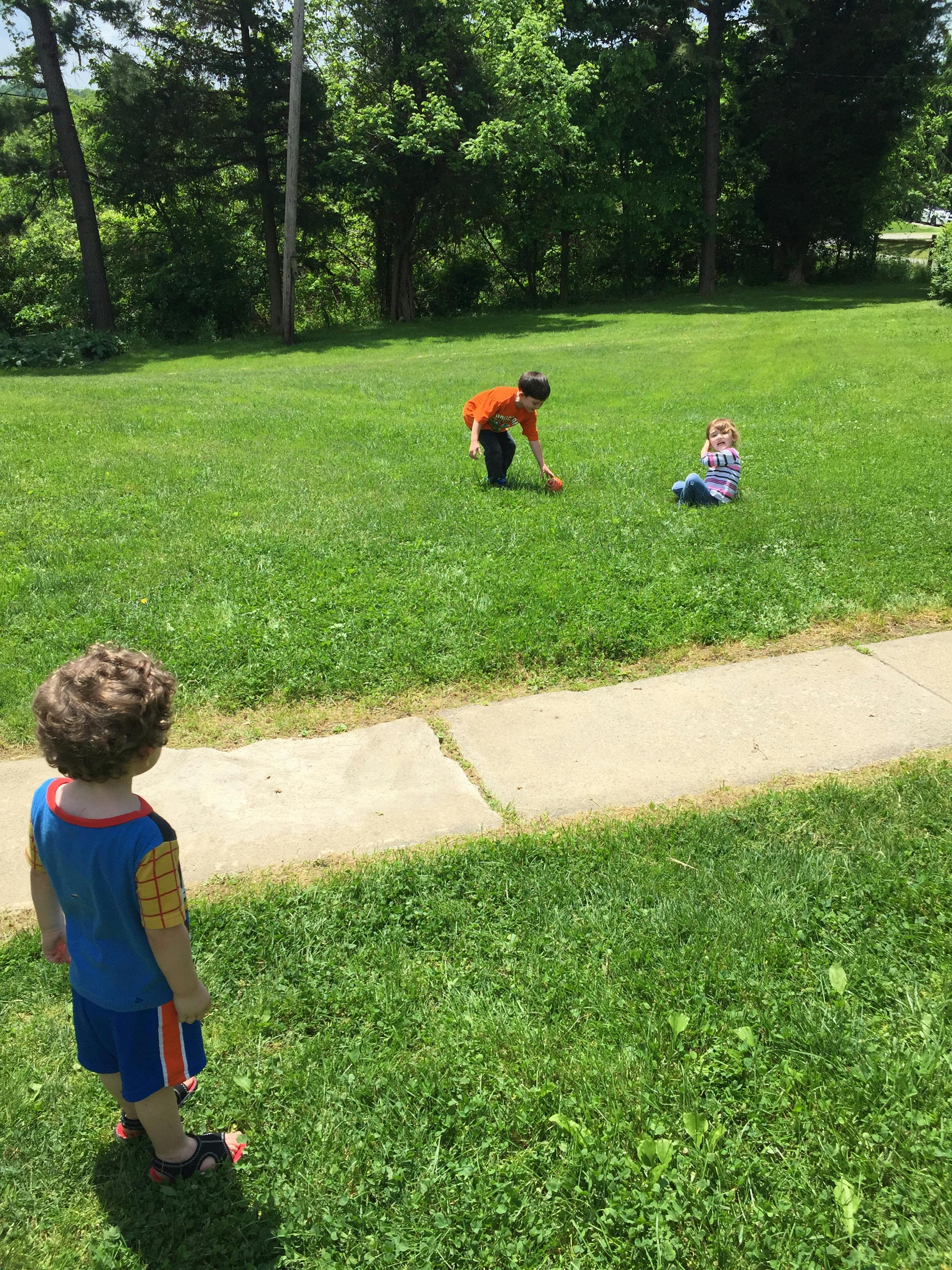 Three children playing in a grassy area
