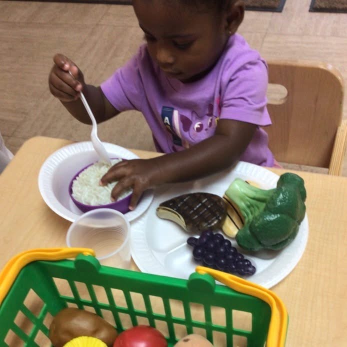 Child playing with toy food, holding a spoon over a bowl of rice