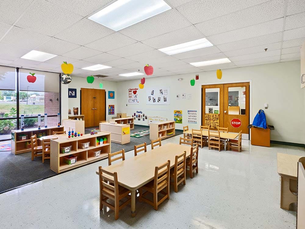 Empty classroom with small wooden tables and chairs, shelves, and apple decorations