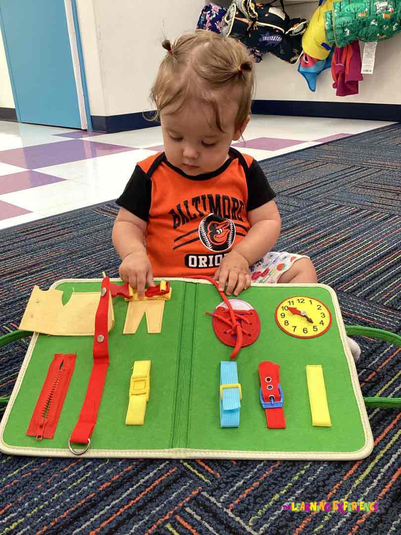 Child playing with a green activity board with various fasteners