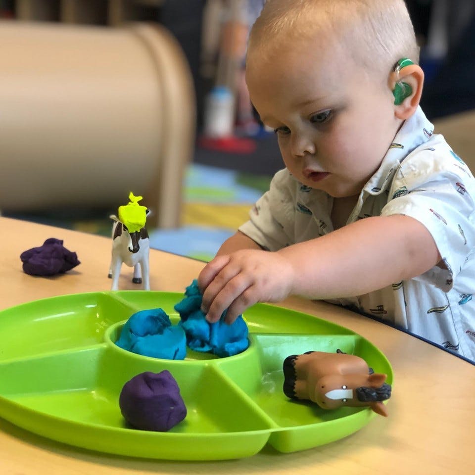 Child playing with modeling clay on a green tray