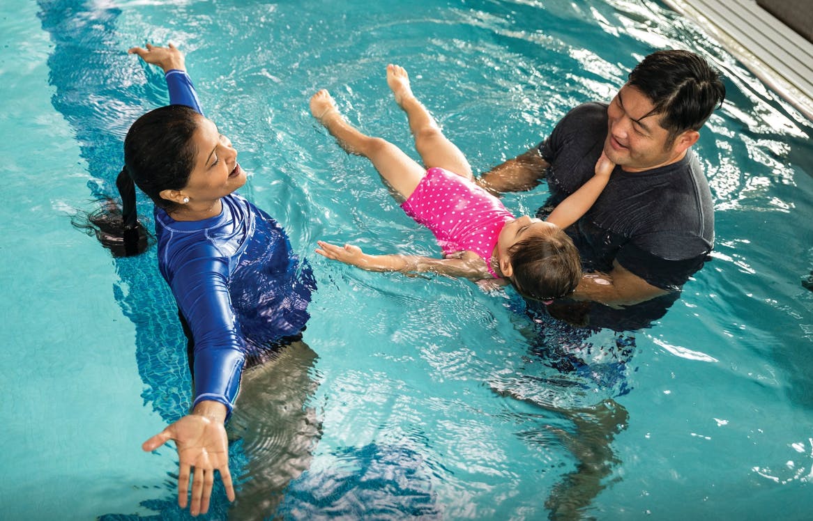 Two people teaching a child to swim in a pool