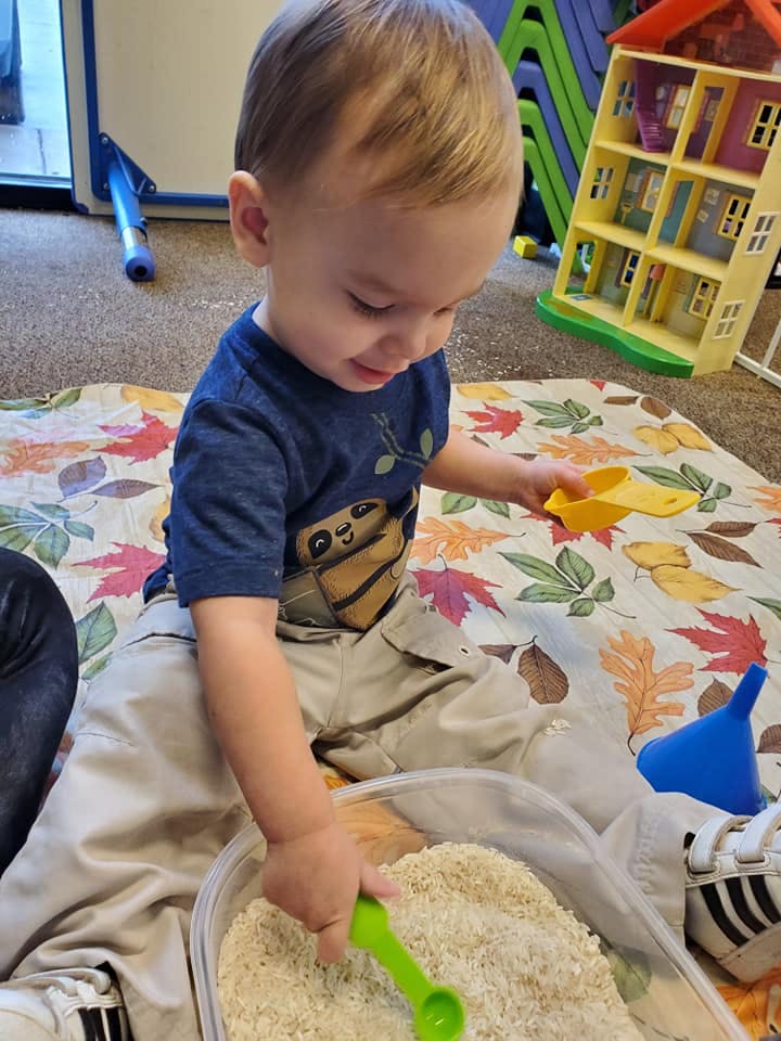 Child playing with rice and a green spoon