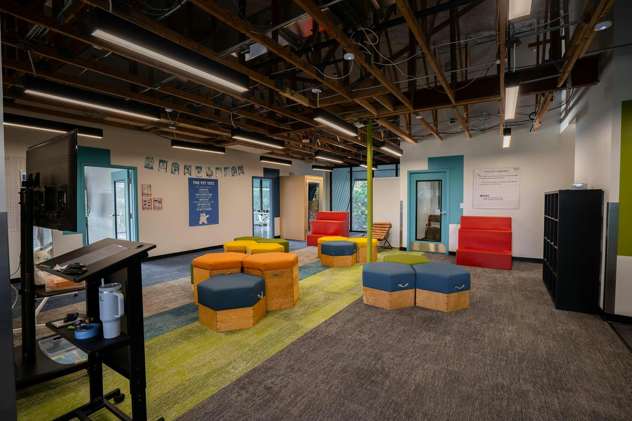 An open plan room with colorful hexagonal ottomans and exposed ceiling beams