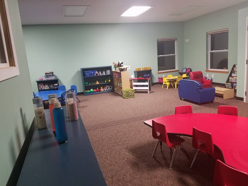 Playroom with red tables and chairs, blue sofa, and shelves with toys