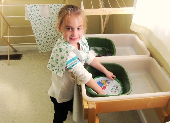Child washing a plate in a tub