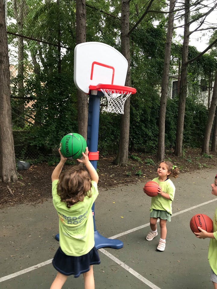 Child shooting a basketball at a hoop, other children holding basketballs