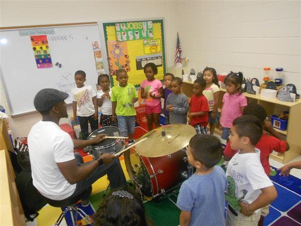 Person playing drums for a group of children in a classroom