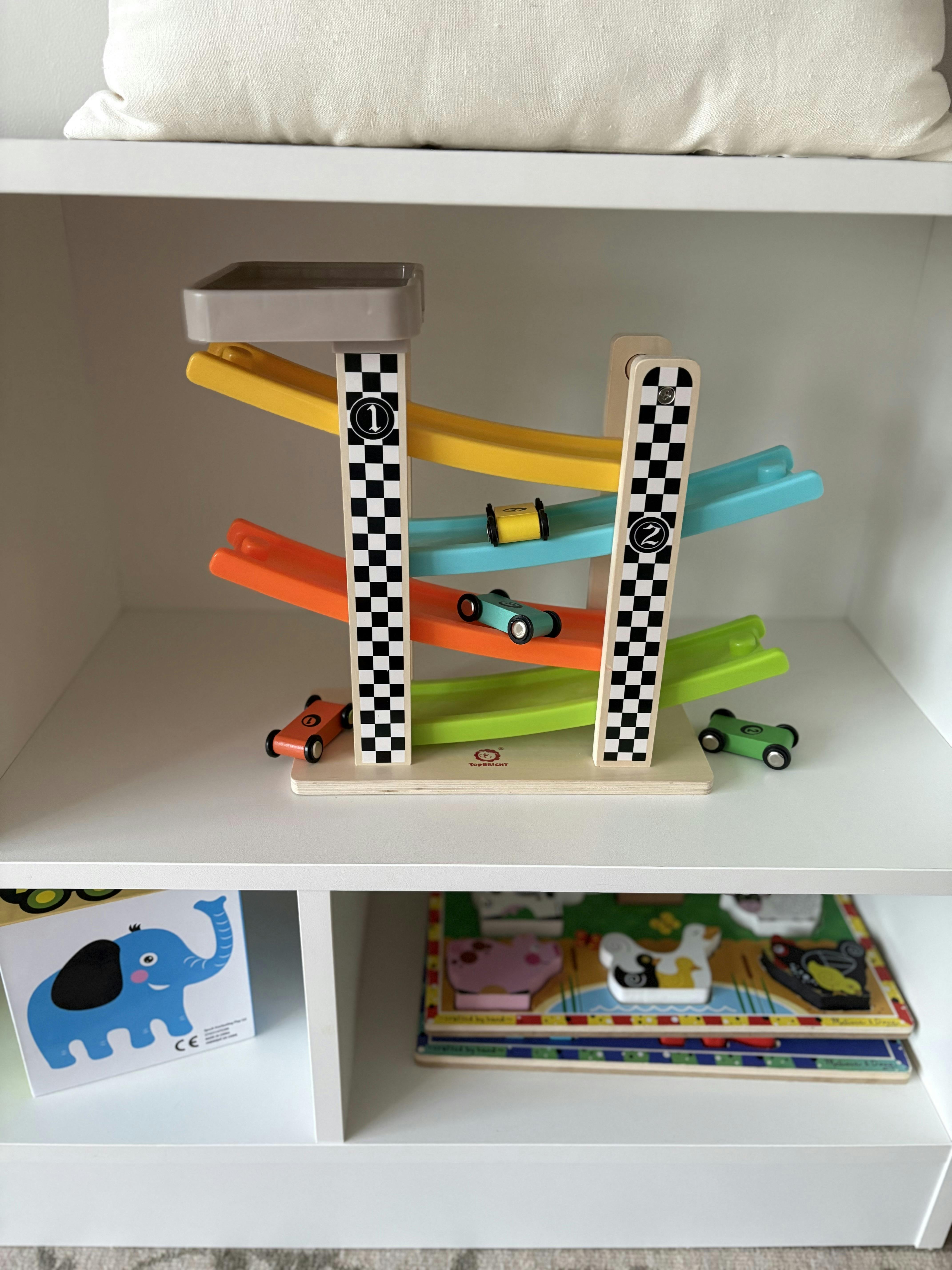 Colorful wooden race track with several toy cars on a white shelf