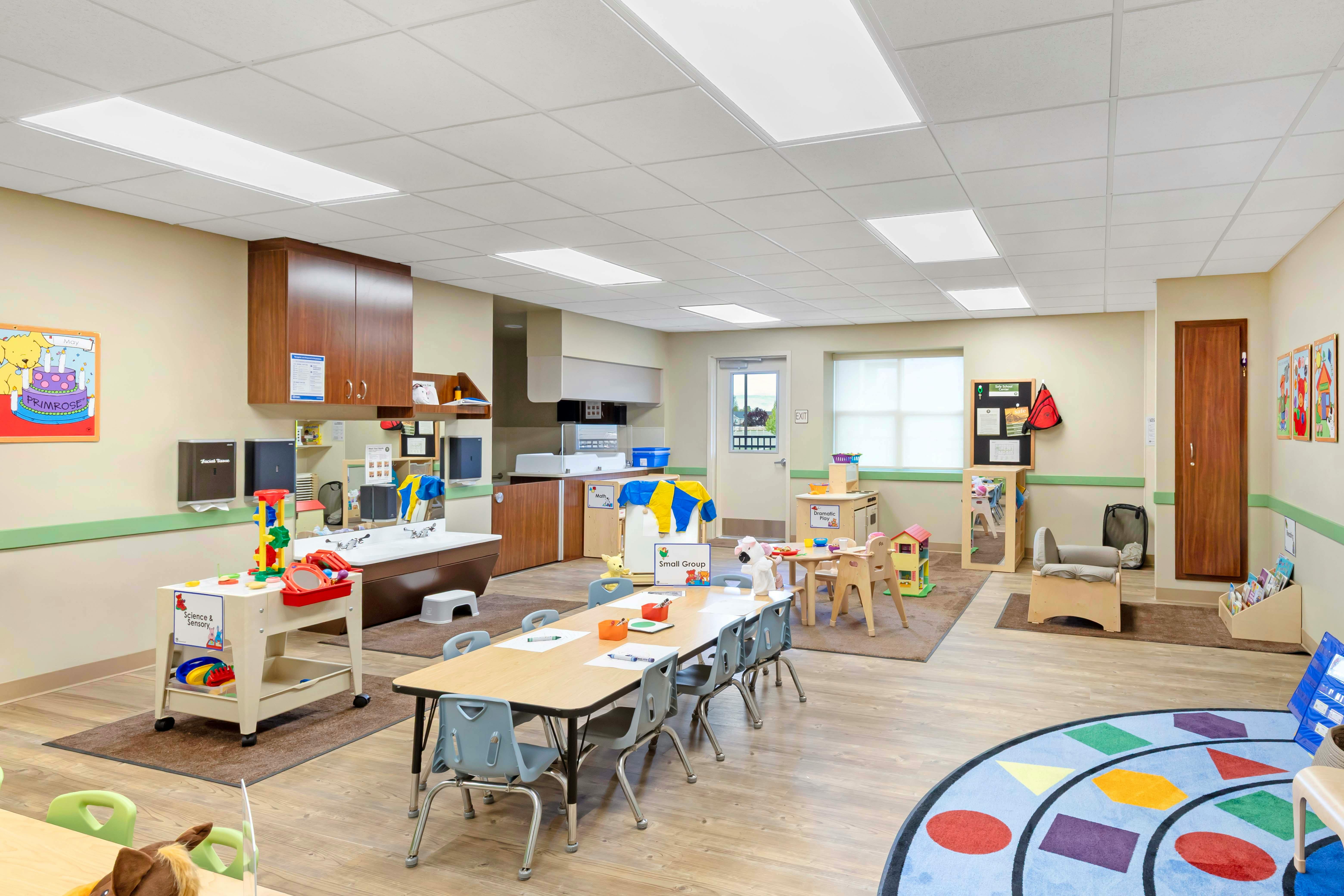 Classroom with child-sized tables and chairs, play kitchen, and sensory table