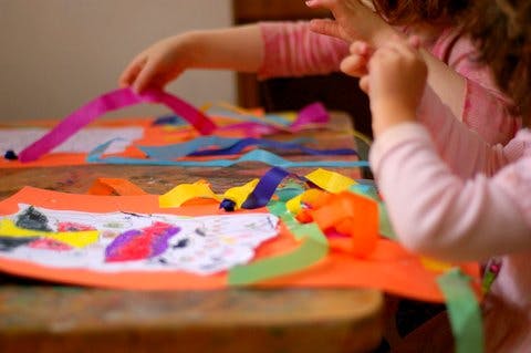 Child's hands working on a craft project with colorful ribbons and paper