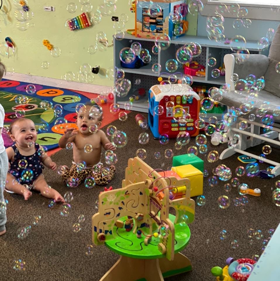 Two babies sitting on a rug surrounded by bubbles