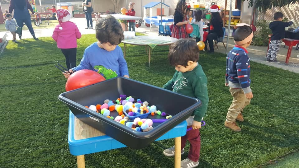 Two children playing with colorful objects in a bin outdoors