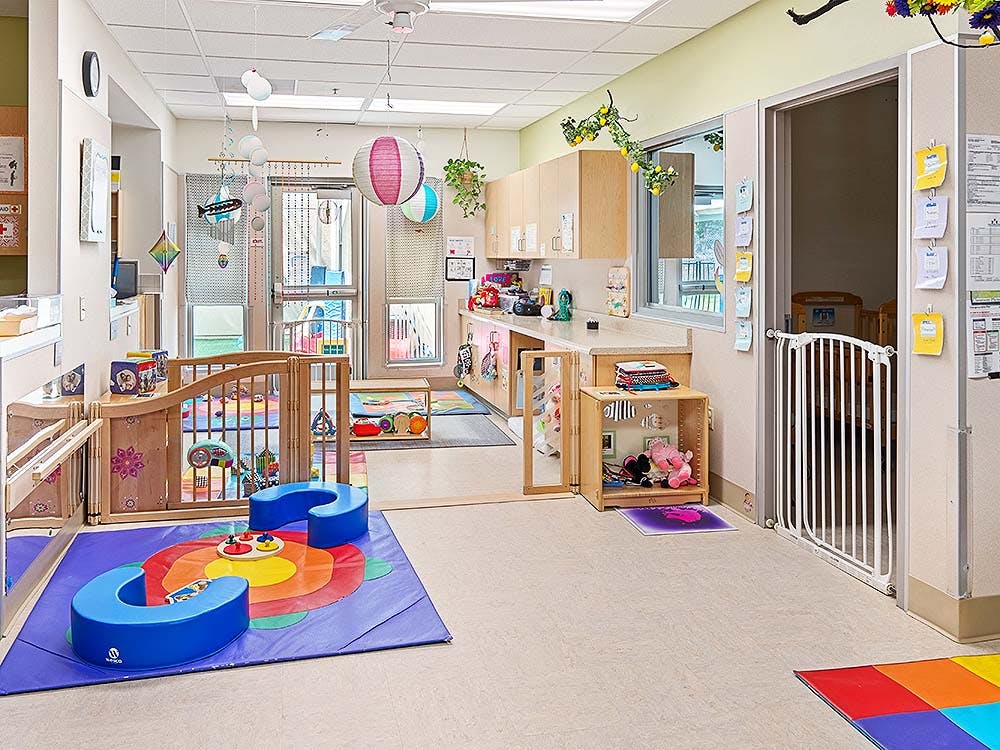 An empty childcare room with play mats, cribs, and colorful decorations
