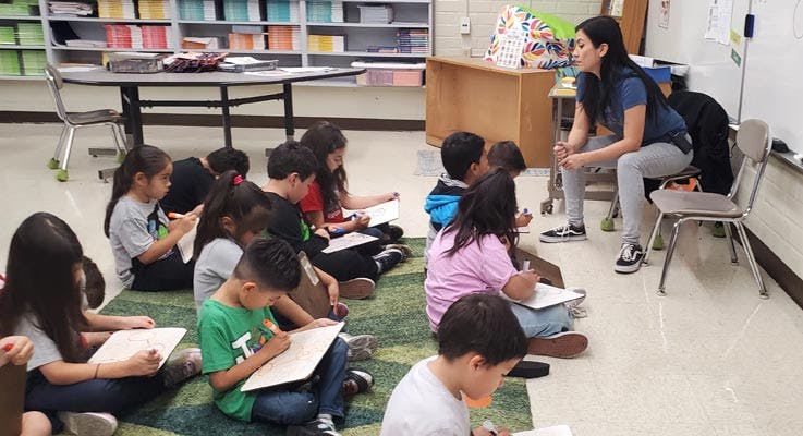 Teacher sitting in front of children drawing on whiteboards in a classroom