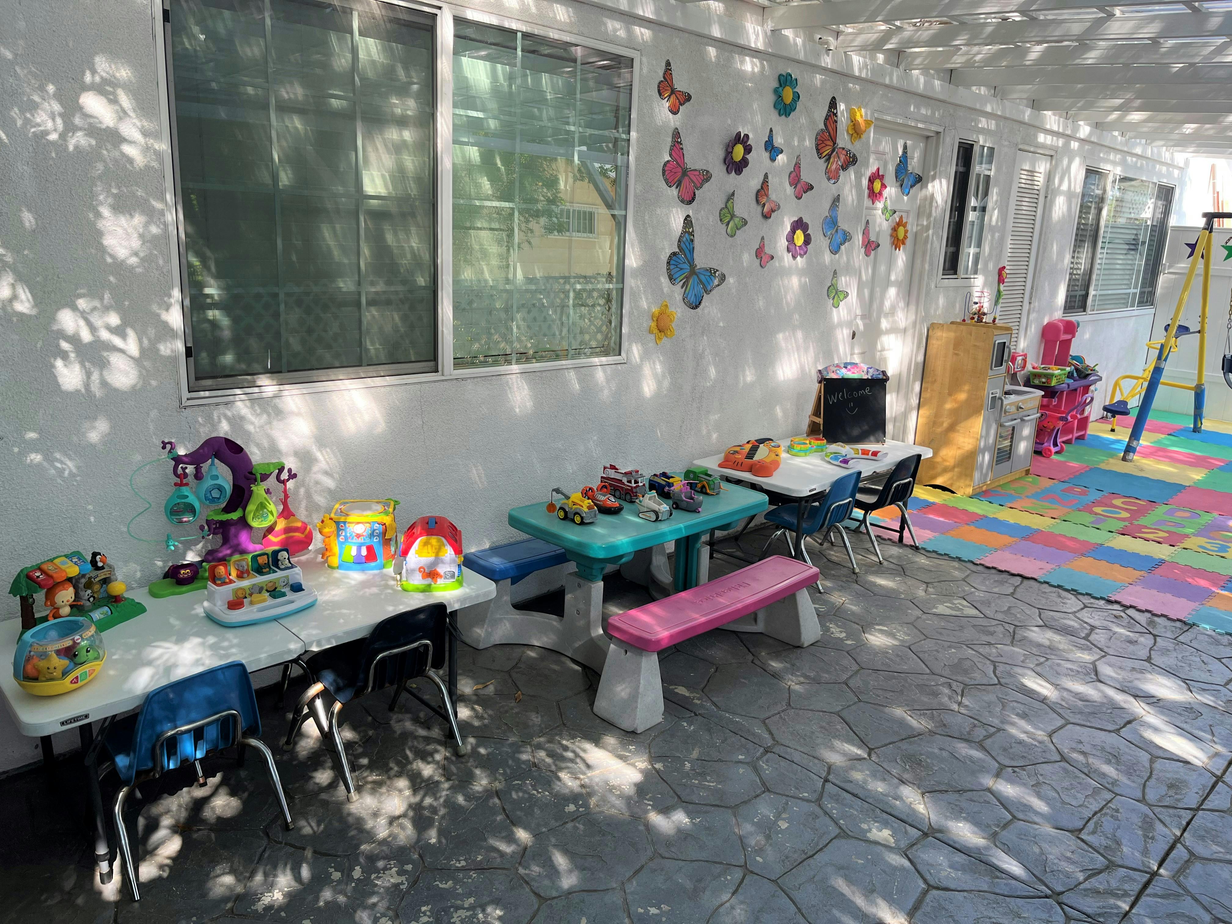 Outdoor play area with small tables, chairs, toys, and a colorful mat