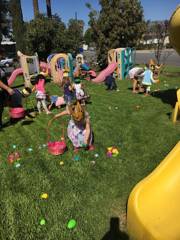 Children collecting eggs on a grassy lawn with playground equipment