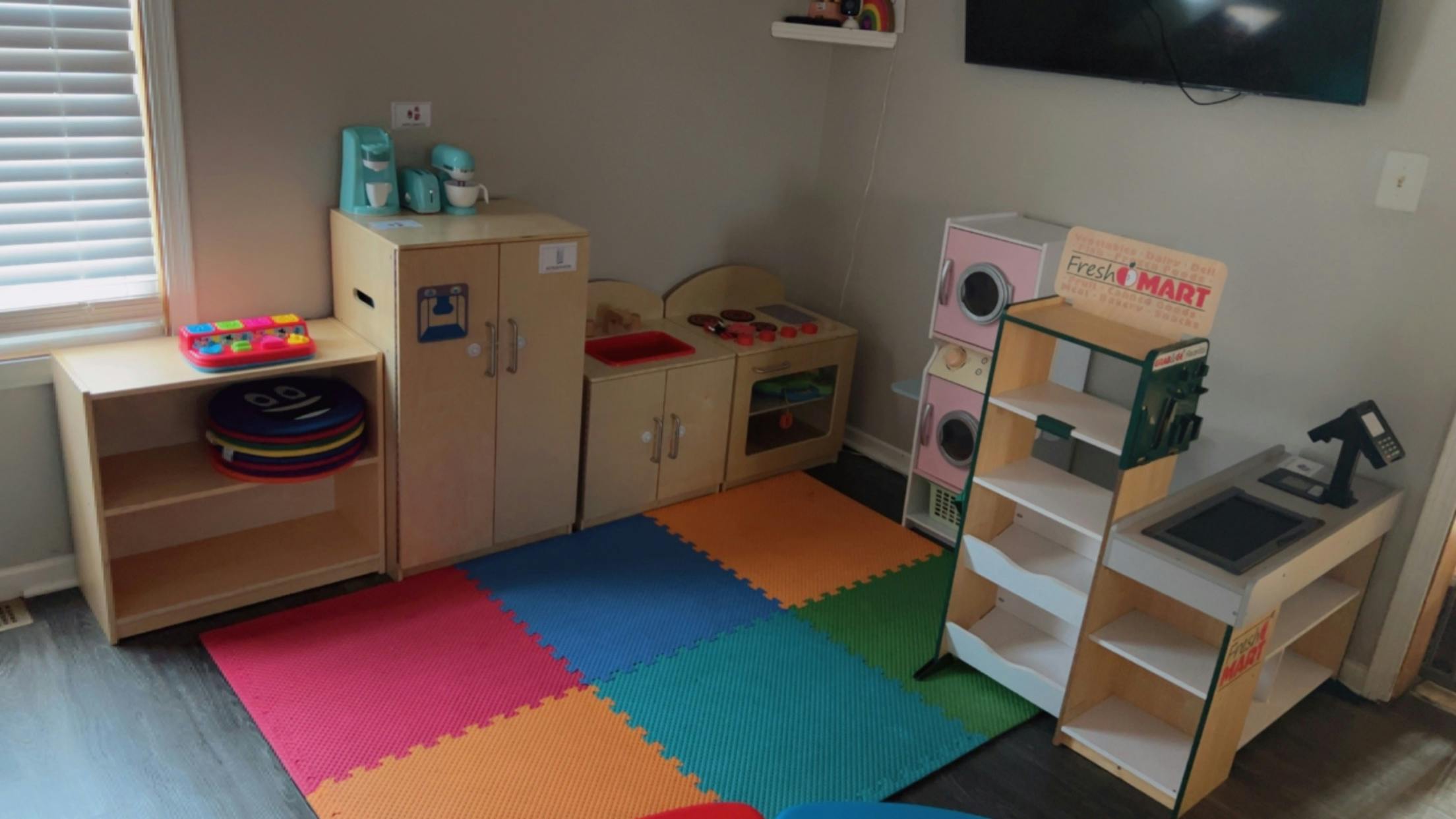 Playroom with colorful floor mats and various wooden toy furniture