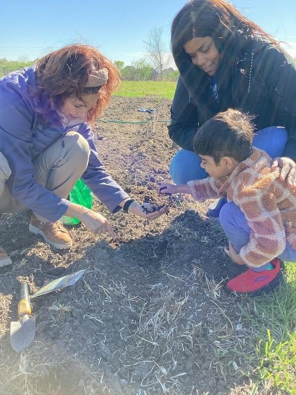 Three people gardening, one holding dirt, another showing dirt to a child