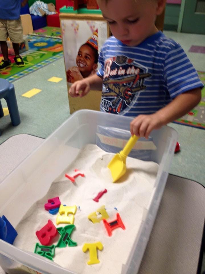 Child playing with a shovel and letter shapes in a sand bin