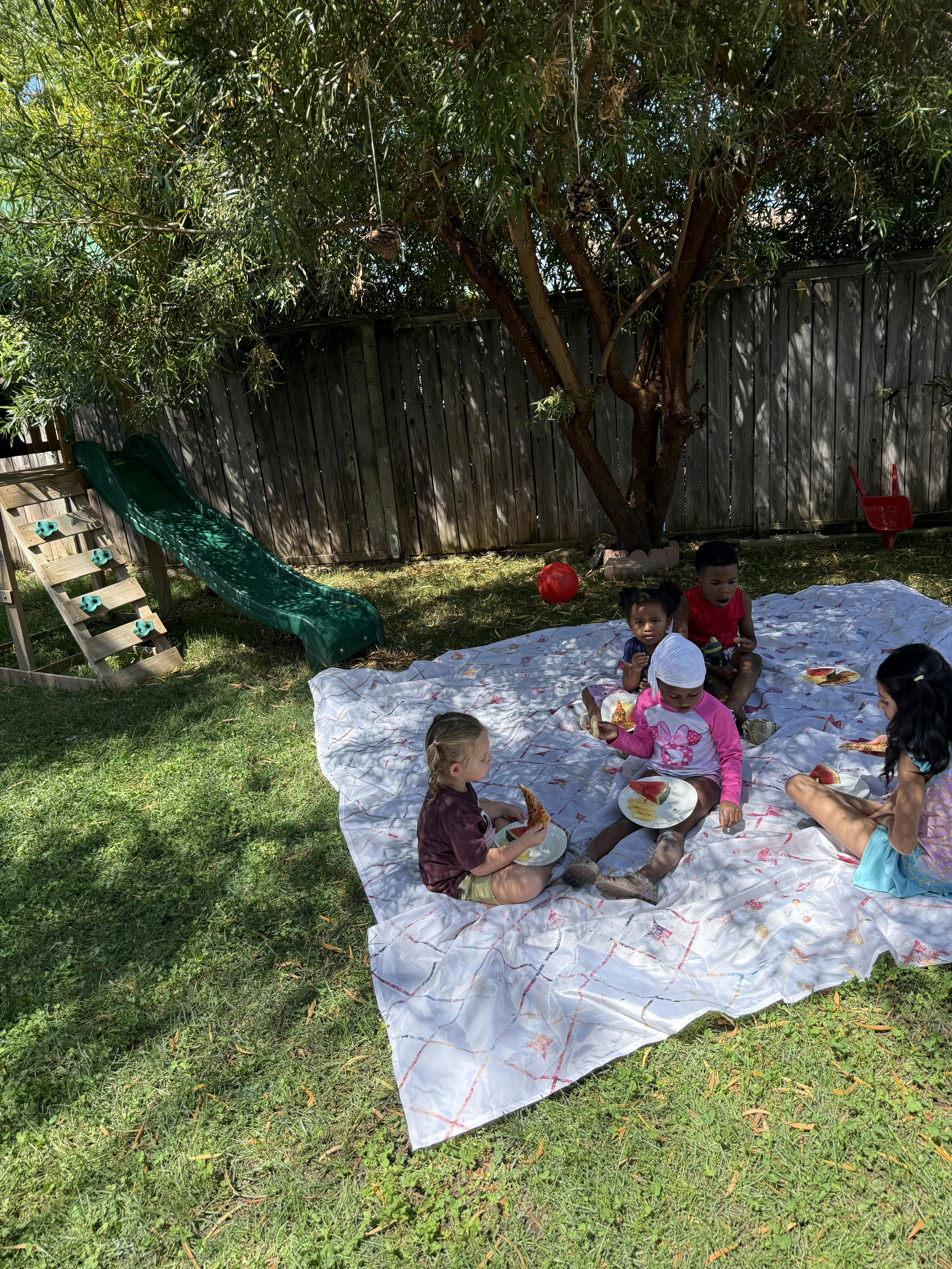 Children eating on a picnic blanket in a backyard