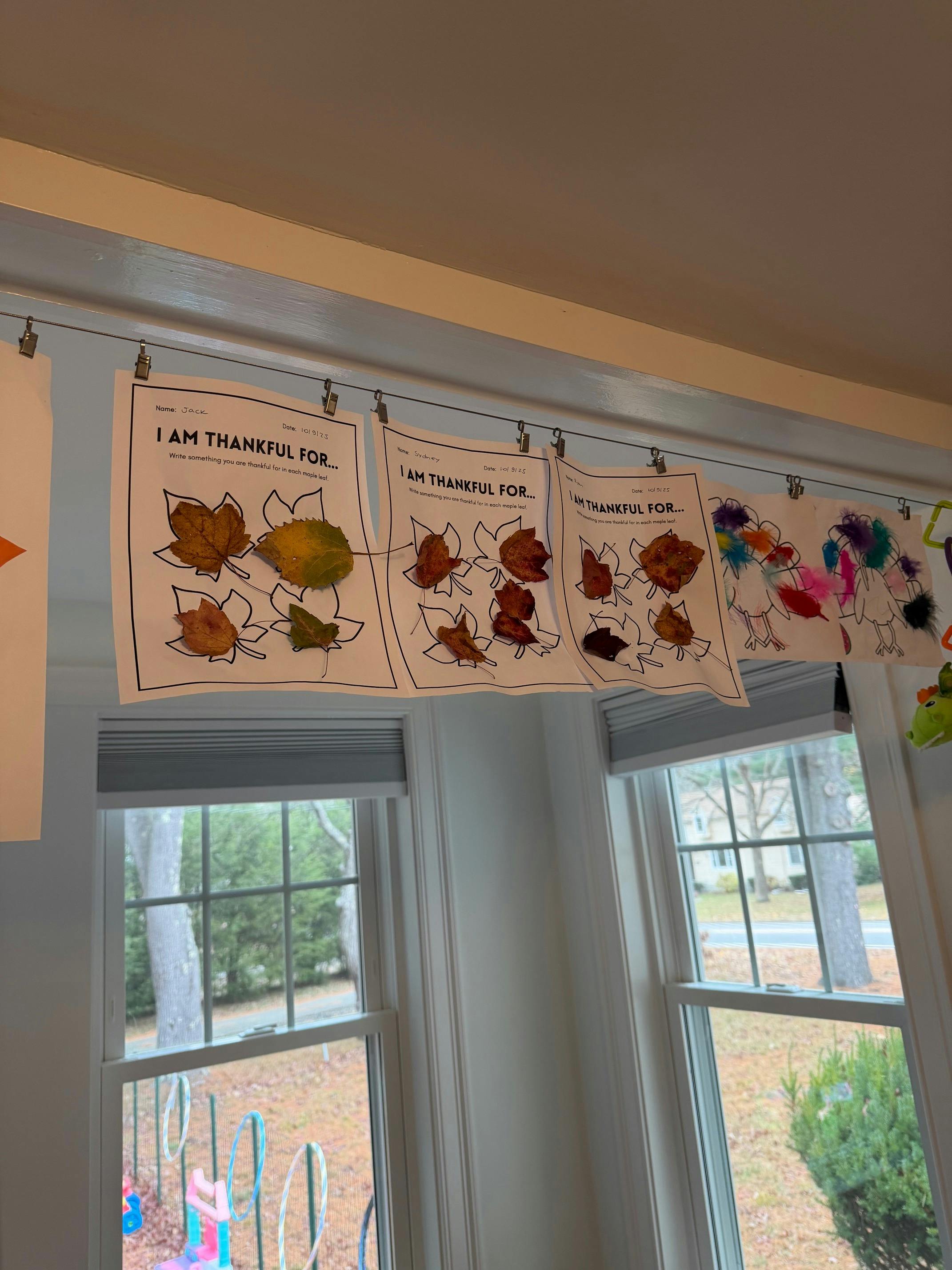 Children's artwork with leaves and text "I AM THANKFUL FOR" hanging above windows