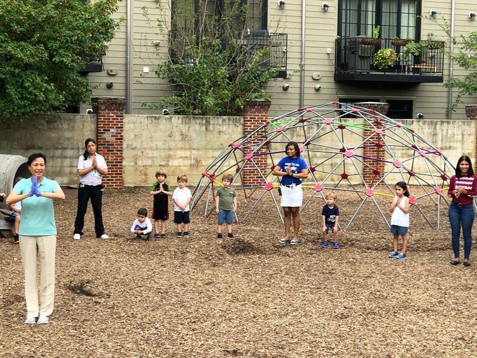 People and children standing in a playground with hands pressed together