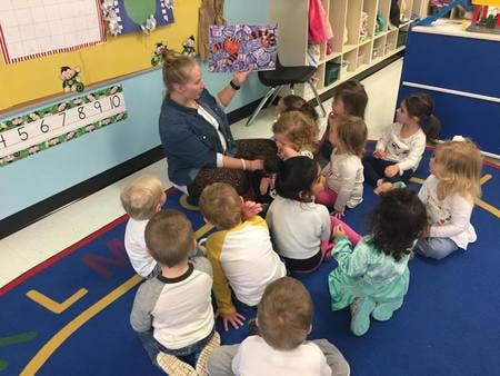 Person reading a book to a group of children in a classroom