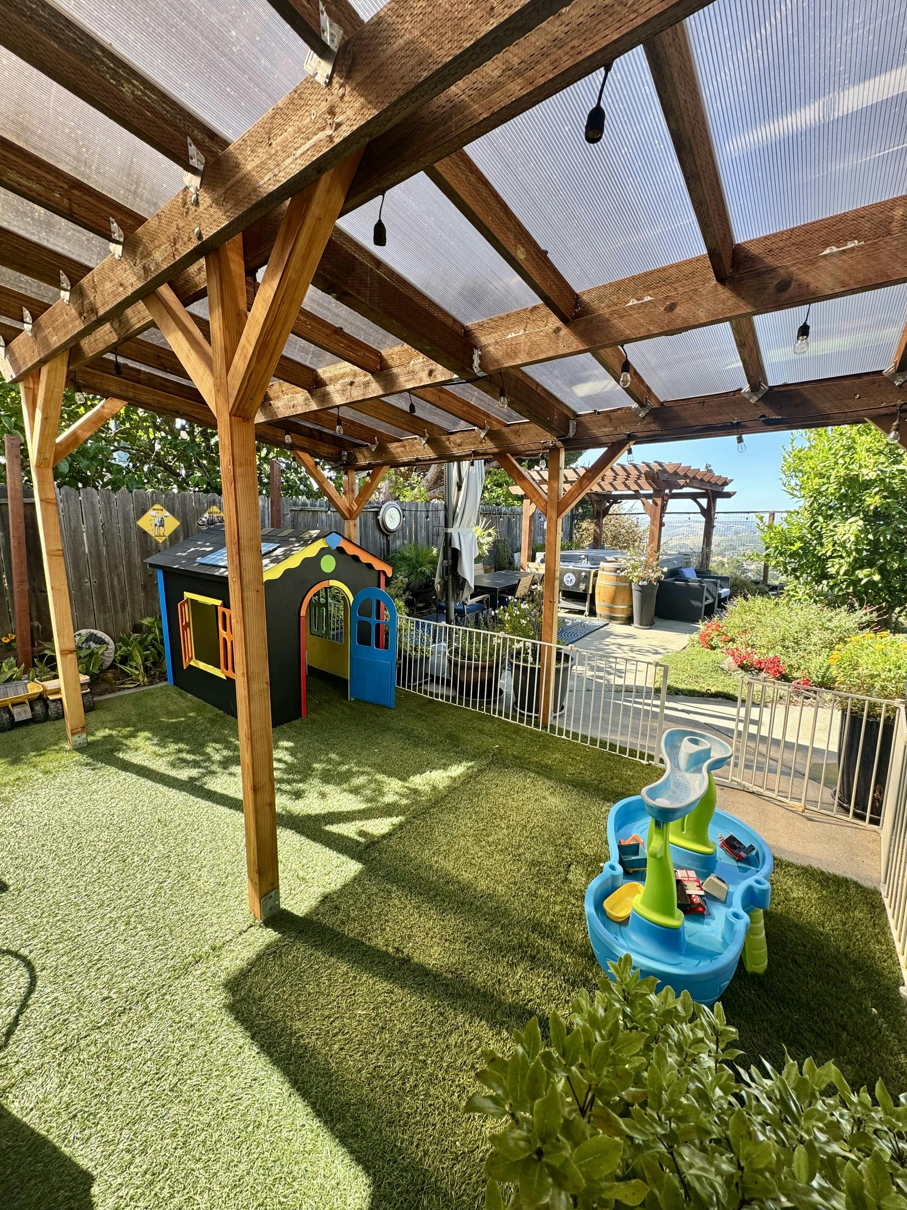 Outdoor play area with a colorful playhouse and water table under a wooden pergola