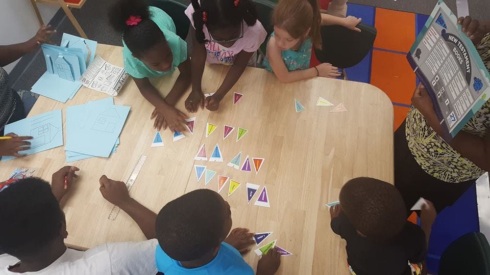 Children and adults at a table with paper and colorful shapes