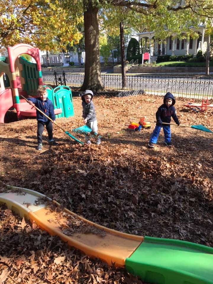 Three children raking leaves in a playground