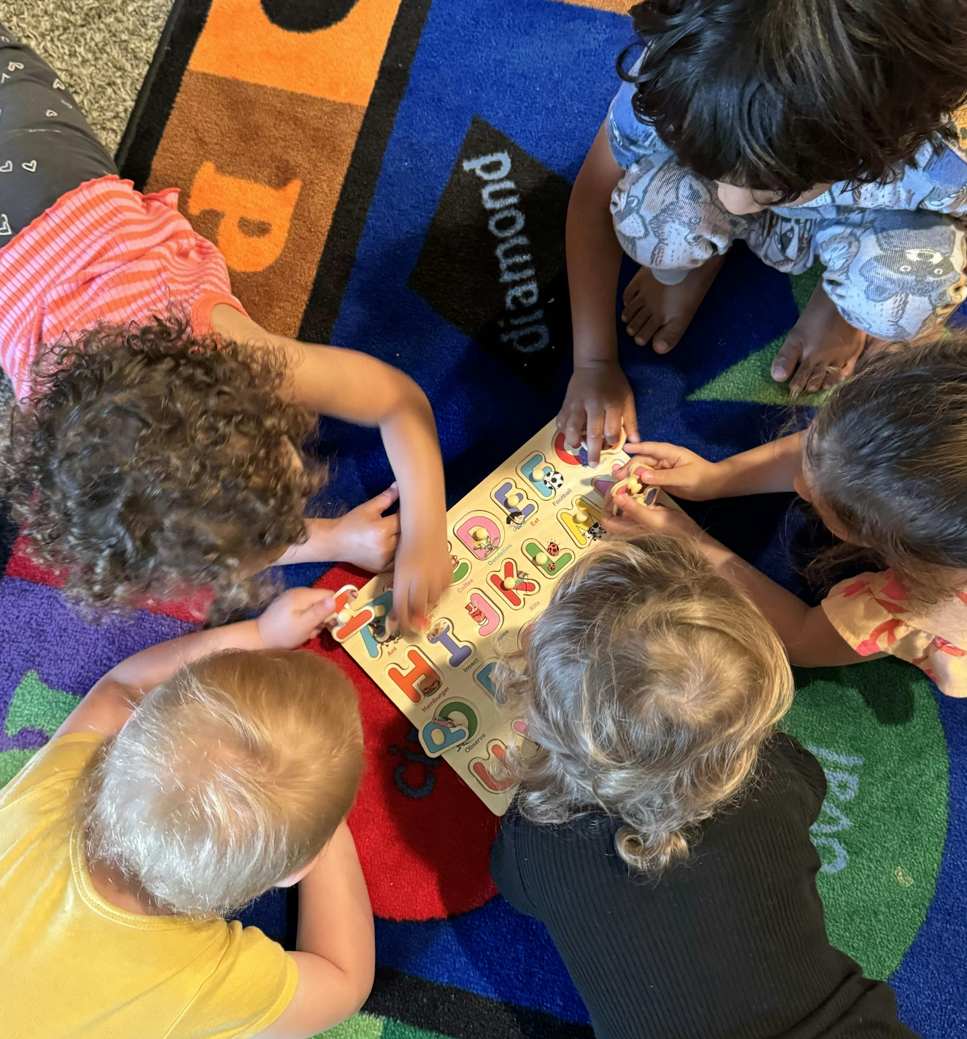 Five children playing with an alphabet puzzle on a colorful rug