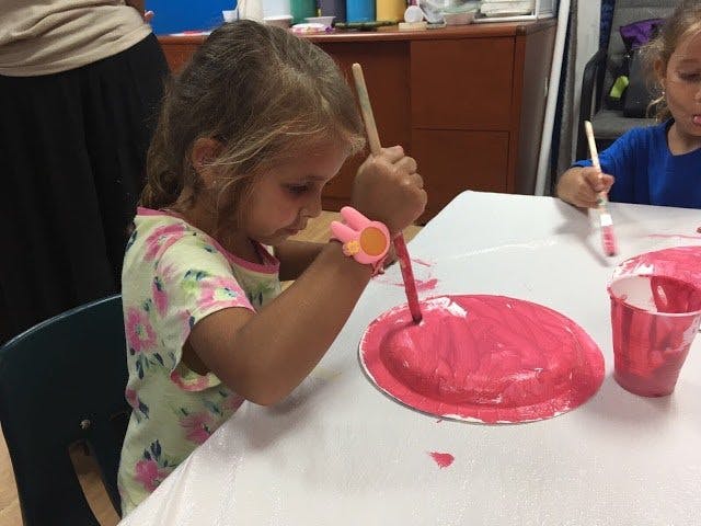 Child painting a paper plate with a brush
