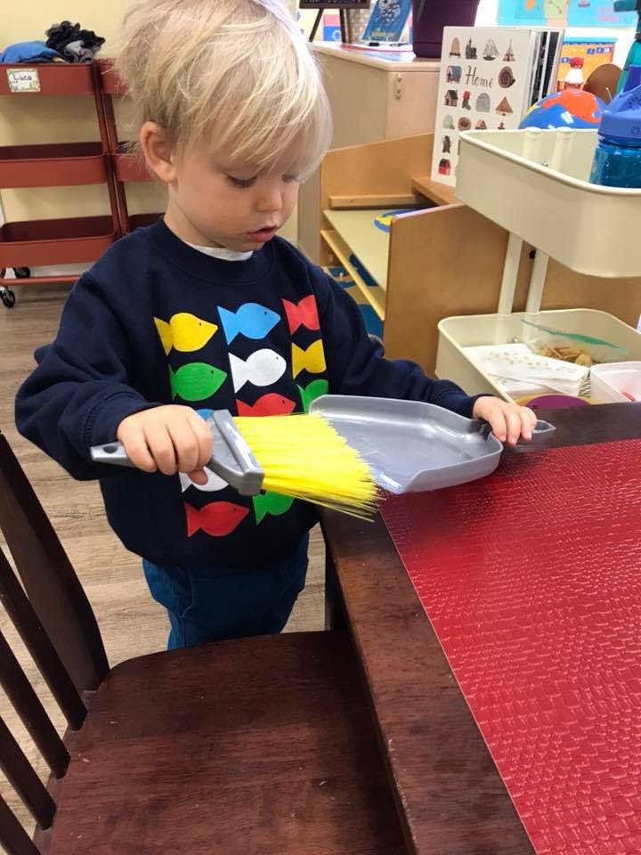 Child sweeping a table with a small broom and dustpan