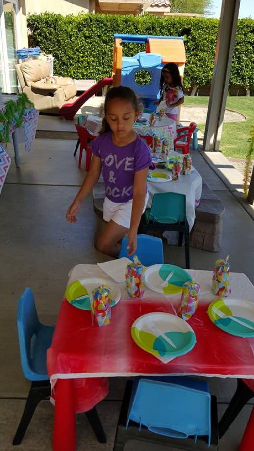 Child kneeling next to a table set with plates and cups