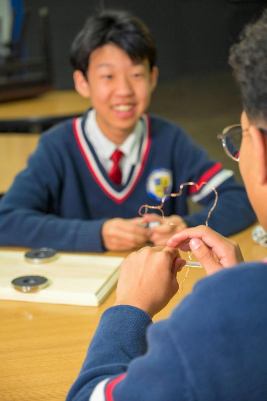 Two teens working with wire, one smiling
