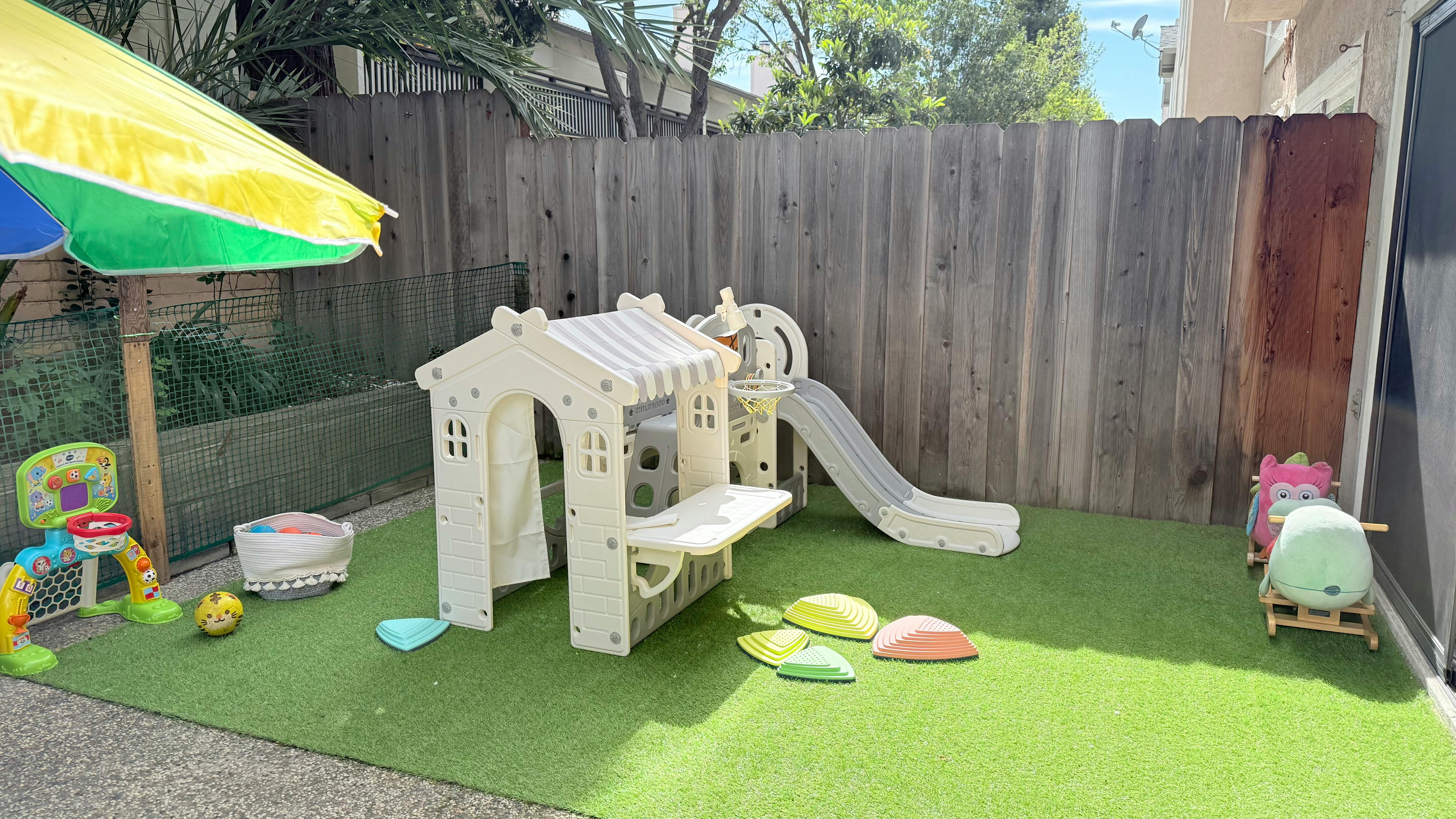 Play area with artificial grass, playhouse, slide, and umbrella
