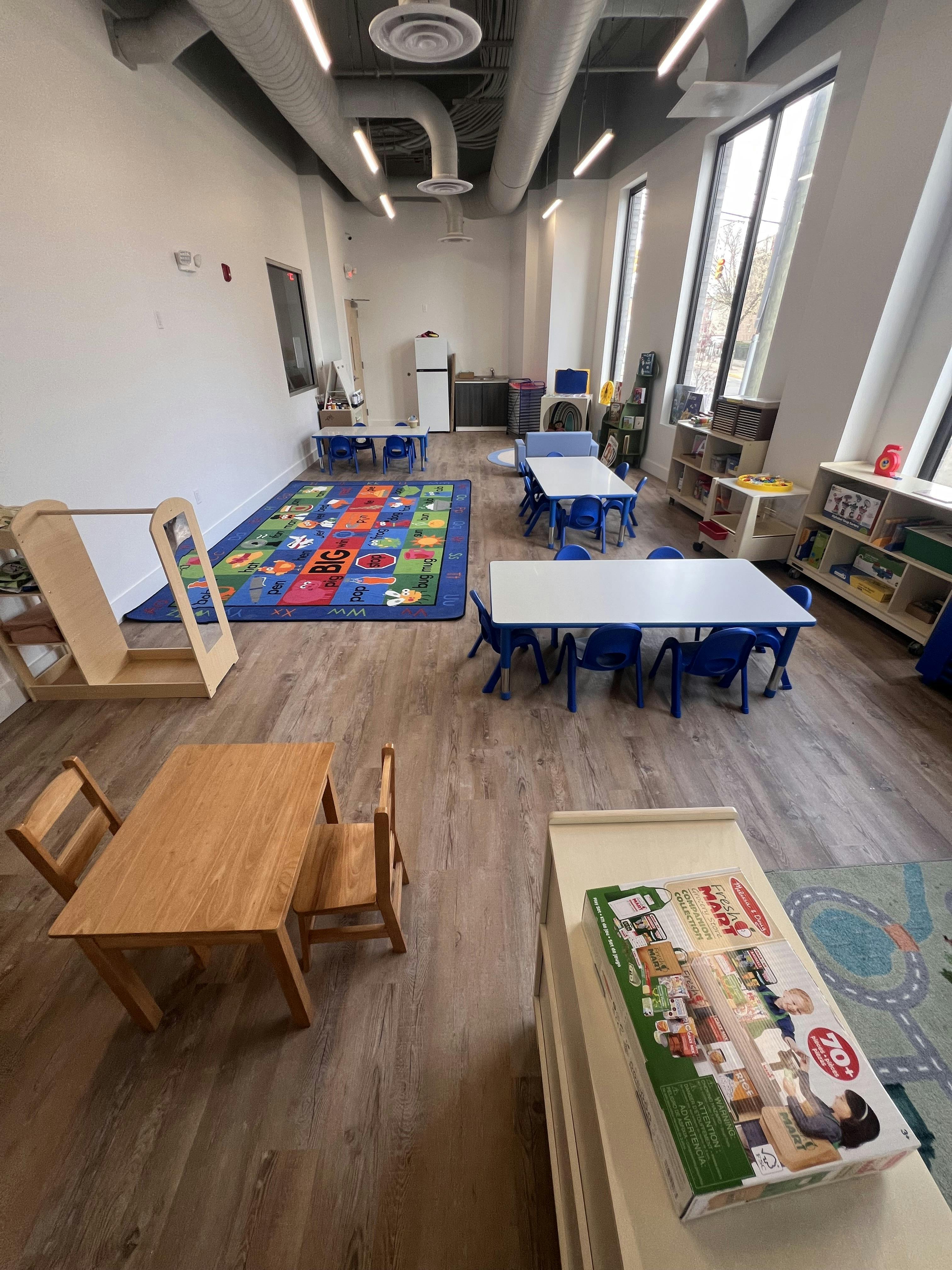 Classroom with small tables and chairs, a colorful alphabet rug, and large windows