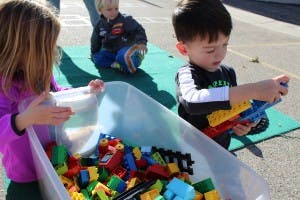 Two children playing with building blocks in a bin outdoors