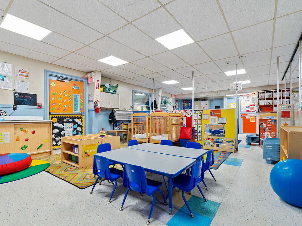Classroom with child-sized tables and chairs, cribs, and colorful decorations
