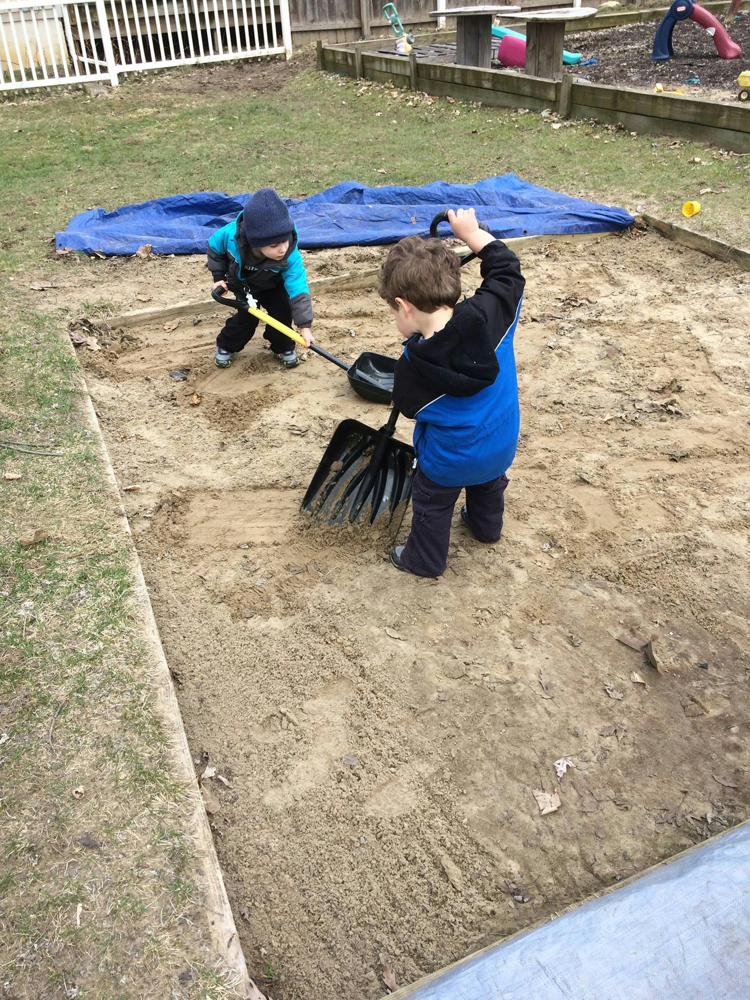 Two children playing in a sandbox with shovels