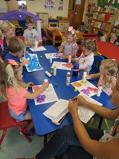 Children and an adult doing crafts at a table in a classroom