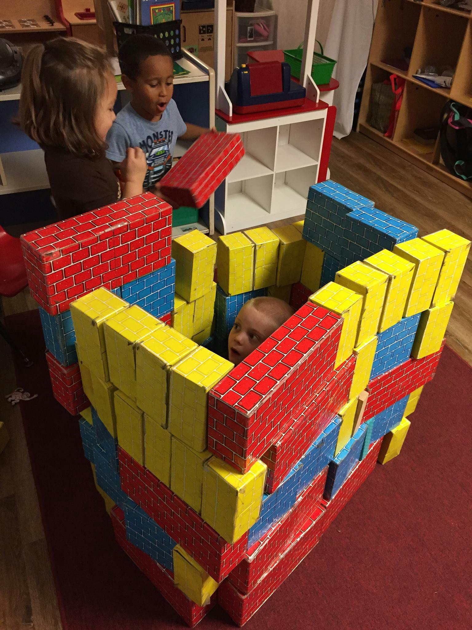 Children playing with large building blocks, one child inside a block structure