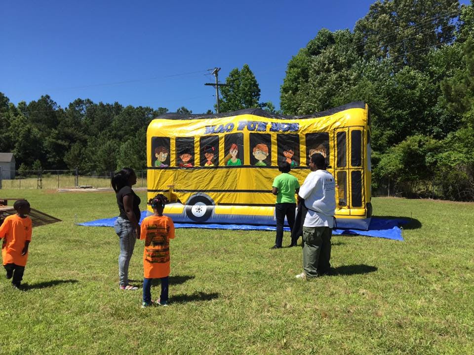 People and children standing near an inflatable yellow school bus bounce house