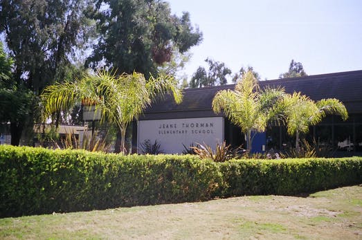 Building with sign "Jane Tuschman Elementary School" behind a hedge