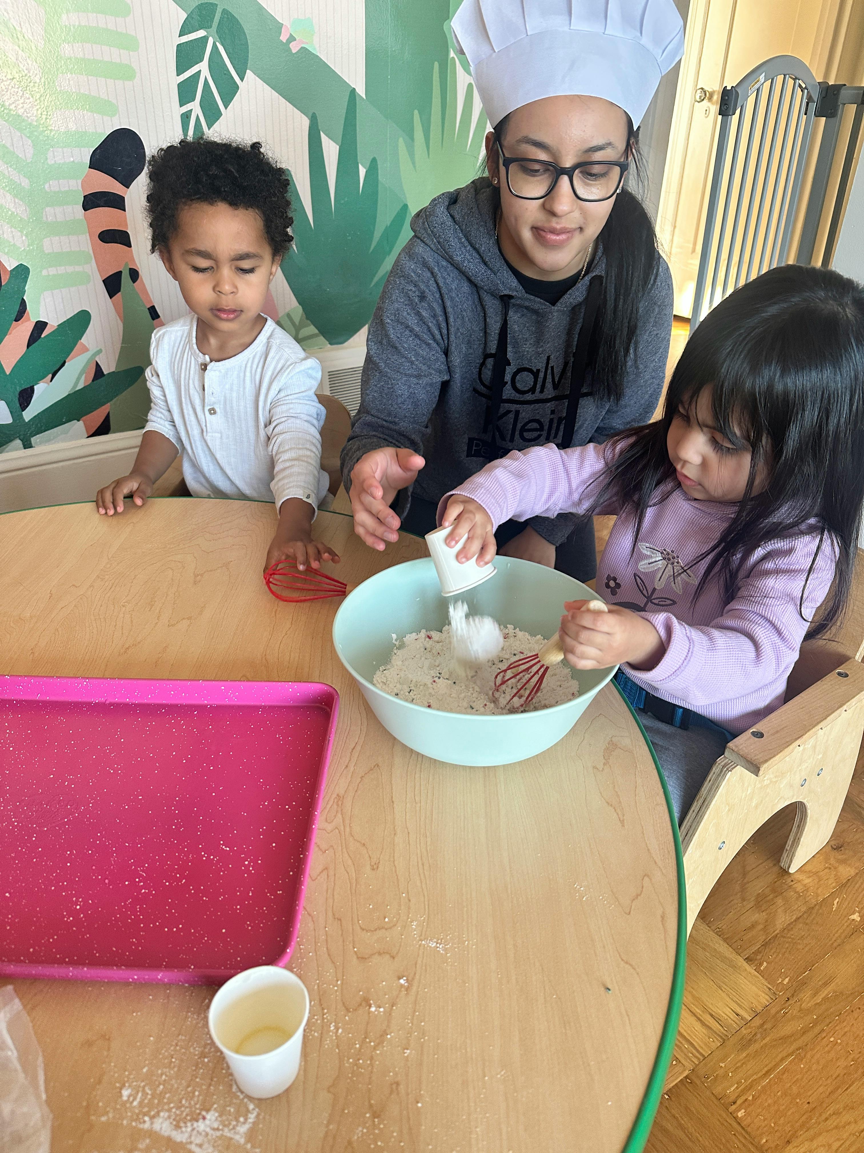 Person in chef hat with two children mixing ingredients in a bowl