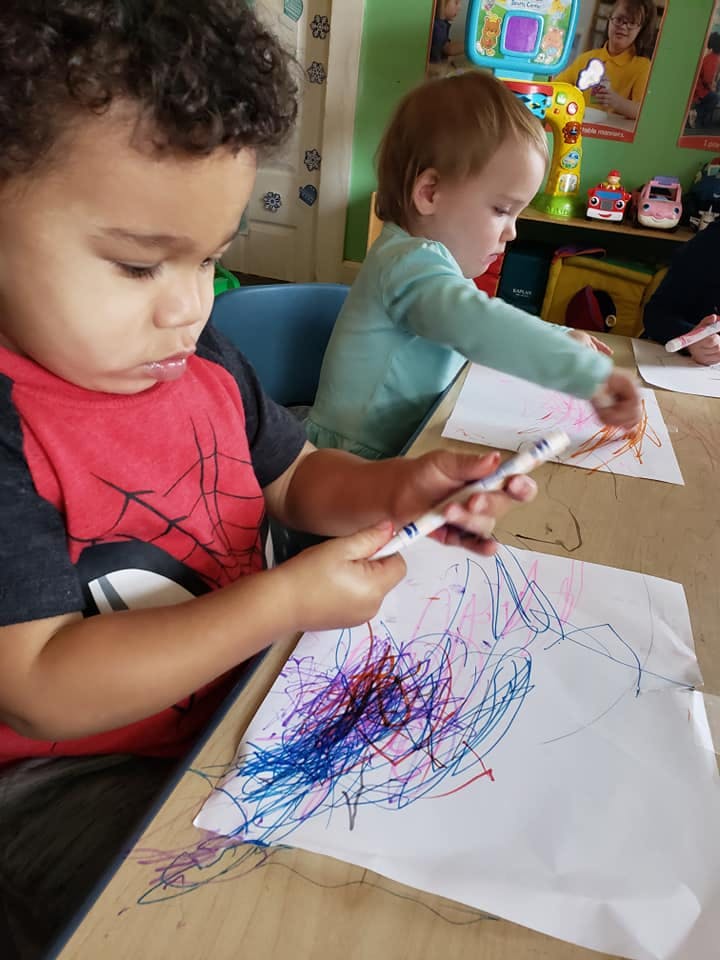 Two children drawing on paper with markers in a classroom