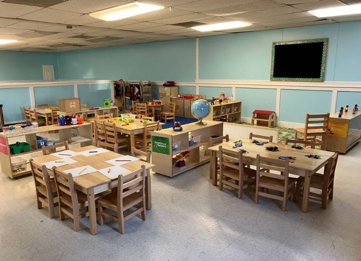 Classroom with wooden tables, chairs, and shelves filled with toys and art supplies