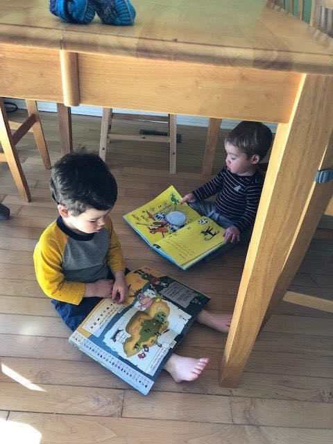Two children sitting on the floor under a table reading books